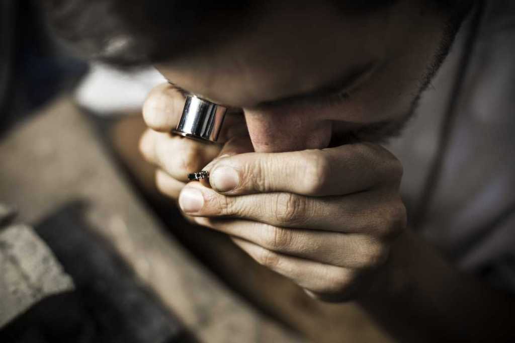 A jeweler closely examines a small ring with a magnifying loupe.