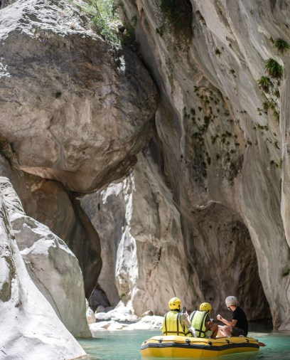 Three people in a yellow raft navigate a turquoise river through towering canyon walls.