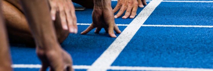 Close-up of sprinters' hands poised on a blue track, lined up at the starting line, ready to race.